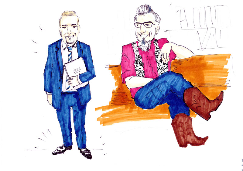 Business-Blau vs. Rockabilly-Rot: SC mit Krawatte und Aktenmappe, TS mit Hosenträgern und Westernboots – zwei Stilwelten auf einer Couch, doch ein Gespräch.