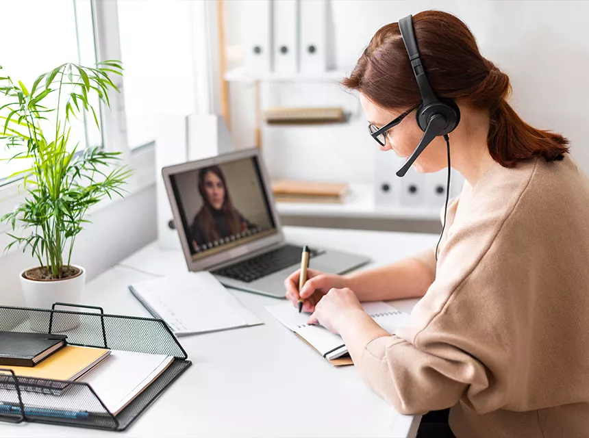 Eine Frau berät eine andere Person per Videocall und schreibt sich dazu Notizen