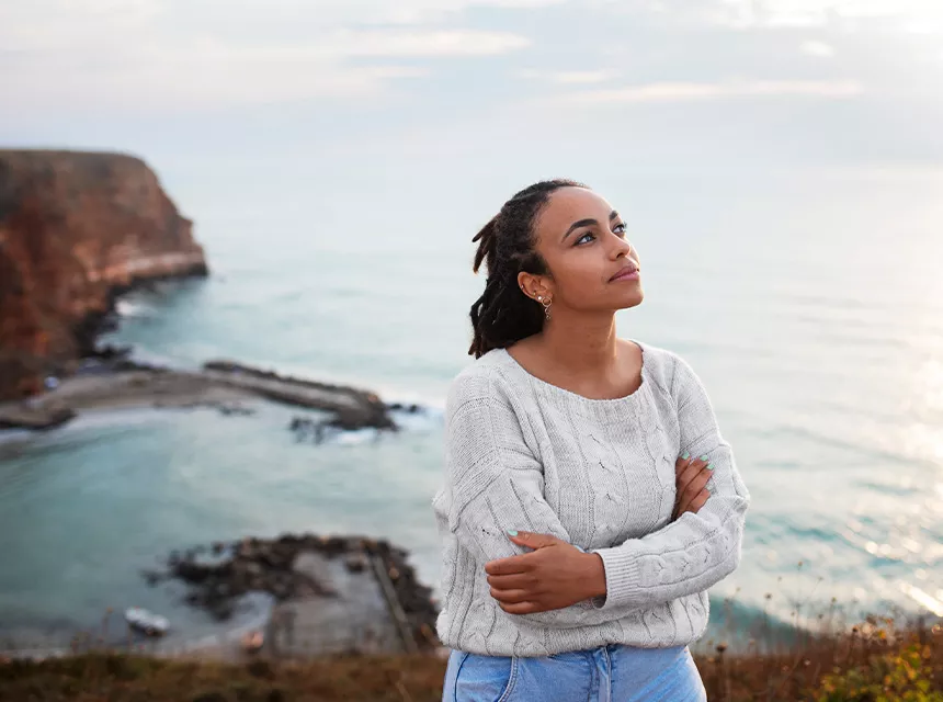 Eine Fnachdenkliche Frau die nach oben blickt, hinter ihr eine Landschaft am Meer