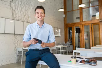 Mann auf Schreibtisch sitzend mit Tablet in der Hand.