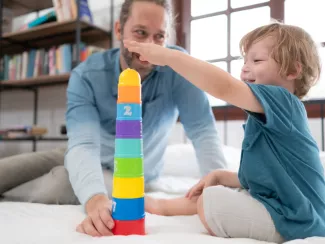 Kind stapelt einen bunten Becherturm mit Hilfe eines jungen Mannes. 