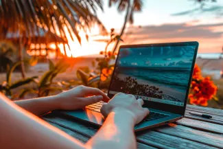 Laptop am Strand im Sonnenuntergang mit Händen, die etwas tippen.