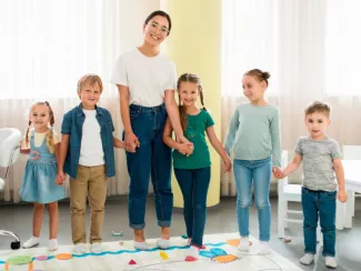 Junge Frau mit Kindern an der Hand in Grundschule oder Kita.