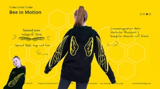 Eine junge Frau trägt einen schwarzen Hoodie mit einem kreativen, bienenartigen Flügelmotiv auf Ärmeln und Rücken auf gelbem Hintergrund. Der Slogan „Spread your wings & hive“ betont die Bedeutung von Bienen und ihrer Rolle im Ökosystem.