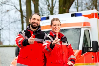 Mann und Frau in DRK-Uniformen mit Daumen hoch vor einem RTW