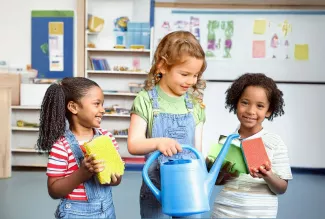 Drei KI-generierte Grundschülerinnen in einem Klassenraum: Sie halten Schwämme und eine Gießkanne und führen spielerisch eine Übung zum Thema Regenwasserversickerung durch.