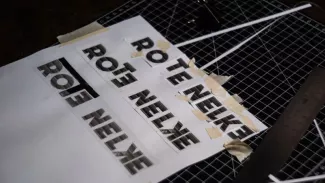 Ausgedruckte und ausgeschnittene Buchstaben für den Titel Rote Nelken liegen mit Klebeband auf einer Schneidematte; die Montage verweist auf den handwerklichen Aufbau des Magazins.