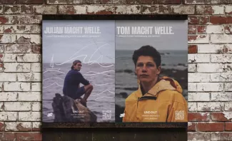 Zwei hochformatige Kampagnenplakate an einer Backsteinwand: Links sitzt ein Mann am Meer, rechts blickt eine Person in gelber Jacke in die Kamera. Beide Plakate tragen den Claim „Mach Welle“ und einen QR-Code.