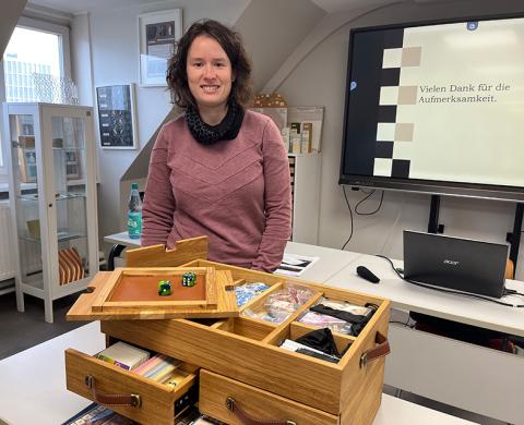 Frau steht hinter einem Werkstück aus Holz und lächelt