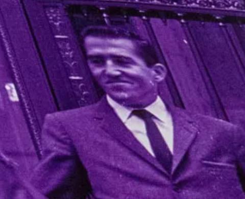 Violett getöntes historisches Foto eines Mannes im Anzug vor einer Tür oder einem Eingang.